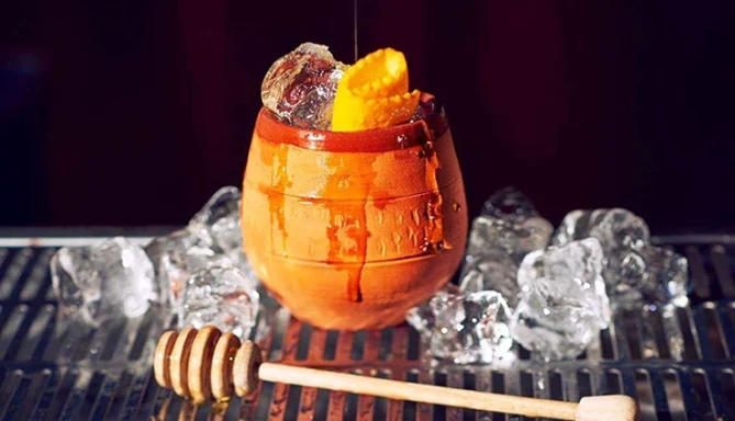 Canchanchara Cocktail avec glaçons, garniture d'orange et miel sur un fond flou.