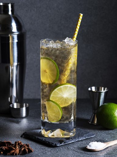 Cocktail avec citron vert et glaçons, shaker en arrière-plan et garniture d'étoile d'anis.