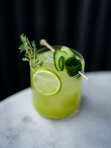 Rhum Cucumbre Cocktail vert avec citron, concombre et herbes, servi dans un verre.