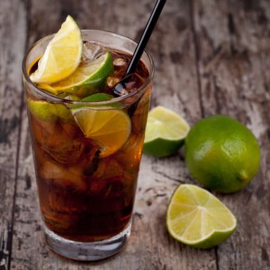 Cuba Libre Un verre de boisson gazeuse avec des quartiers de citron vert sur une table en bois.