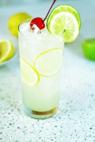 Tom Collins Un verre de limonade avec des tranches de citron, cerise rouge et glaçons.