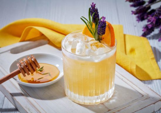 Bee's Knees Cocktail agrume avec glace, garniture de lavande et miel sur un plateau avec serviette jaune.