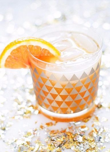 Happy Ending Cocktail dans un verre décoré, garni d'une tranche d'orange sur un fond festif.