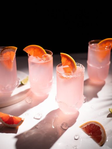 PALOMA Quatre verres de cocktail rose garnis d'une rondelle d'orange sur une table.