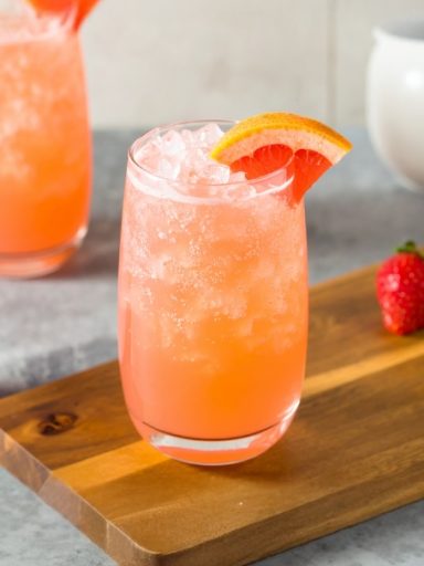 Pink Elephant Verre de boisson rose, glacé, décoré d'une tranche d'orange et un fraisier à côté.